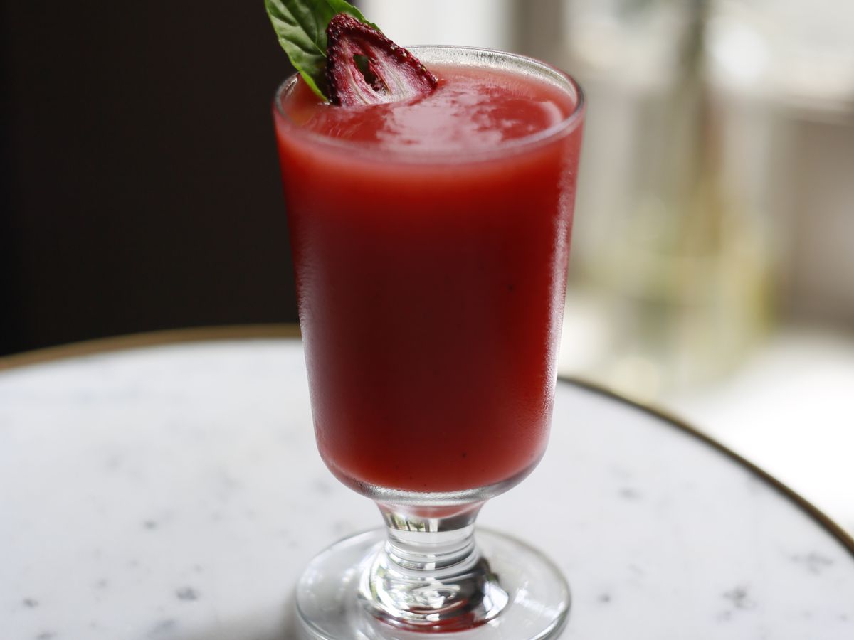 A red frozen cocktail with strawberry and mint garnish set on a white marble table.