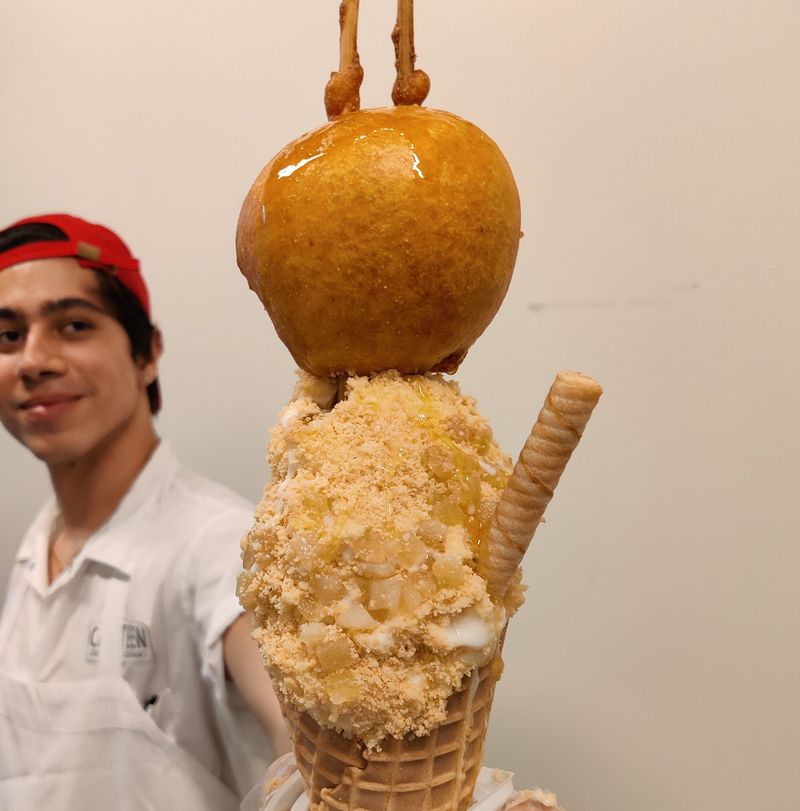 A staffer holds out a cone topped with a caramel apple and crumbles. 