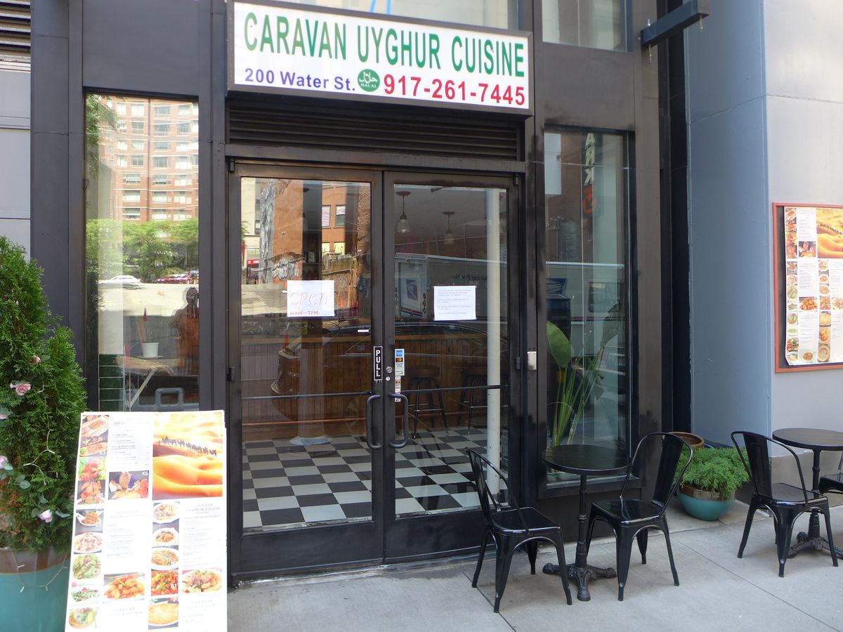A blue sign above a black metal door with a propped up giant menu on the left side.