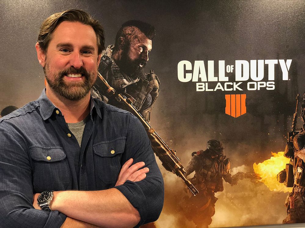 A photo of Treyarch’s Dan Bunting in front of artwork for Call of Duty: Black Ops 4