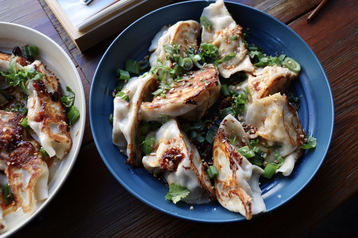 A bowl of dumplings with scallion, cilantro, fried garlic, and chili oil.
