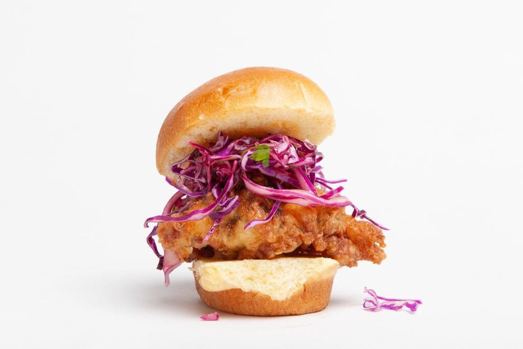 A fried chicken sandwich with purple cabbage coleslaw and a large piece of chicken. 