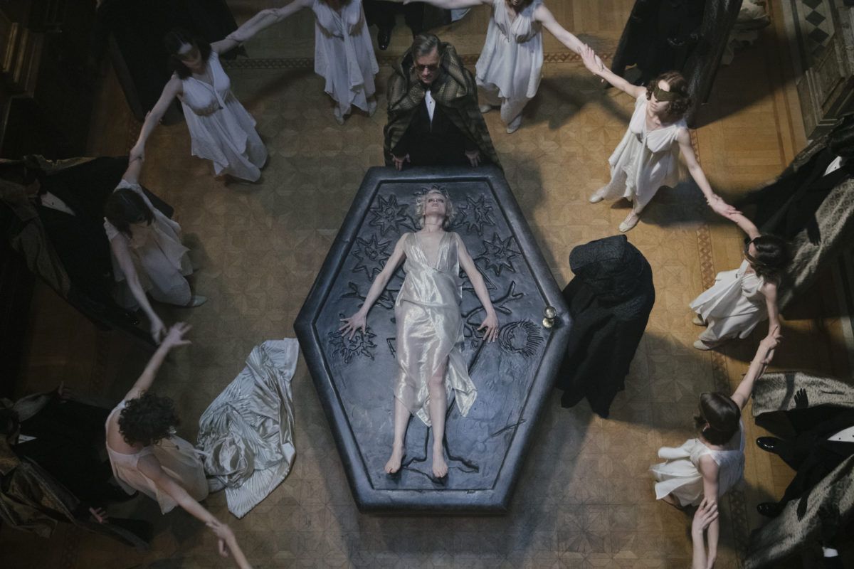 A group of blindfolded women in white joining hands around a woman in a silk white dress lying on an altar with two men standing over her in dark robes in a still from Babylon Berlin season 3