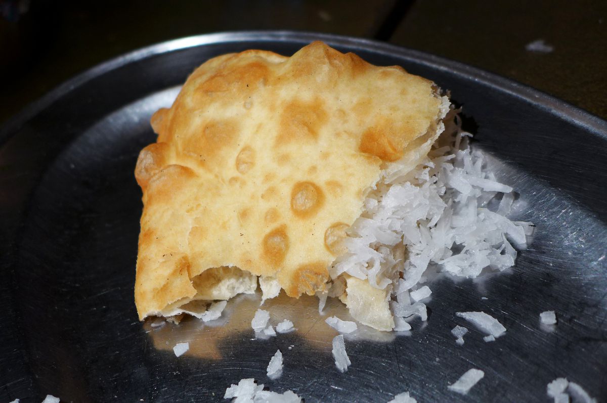 A torn flatbread spills white coconut onto a metal tray.