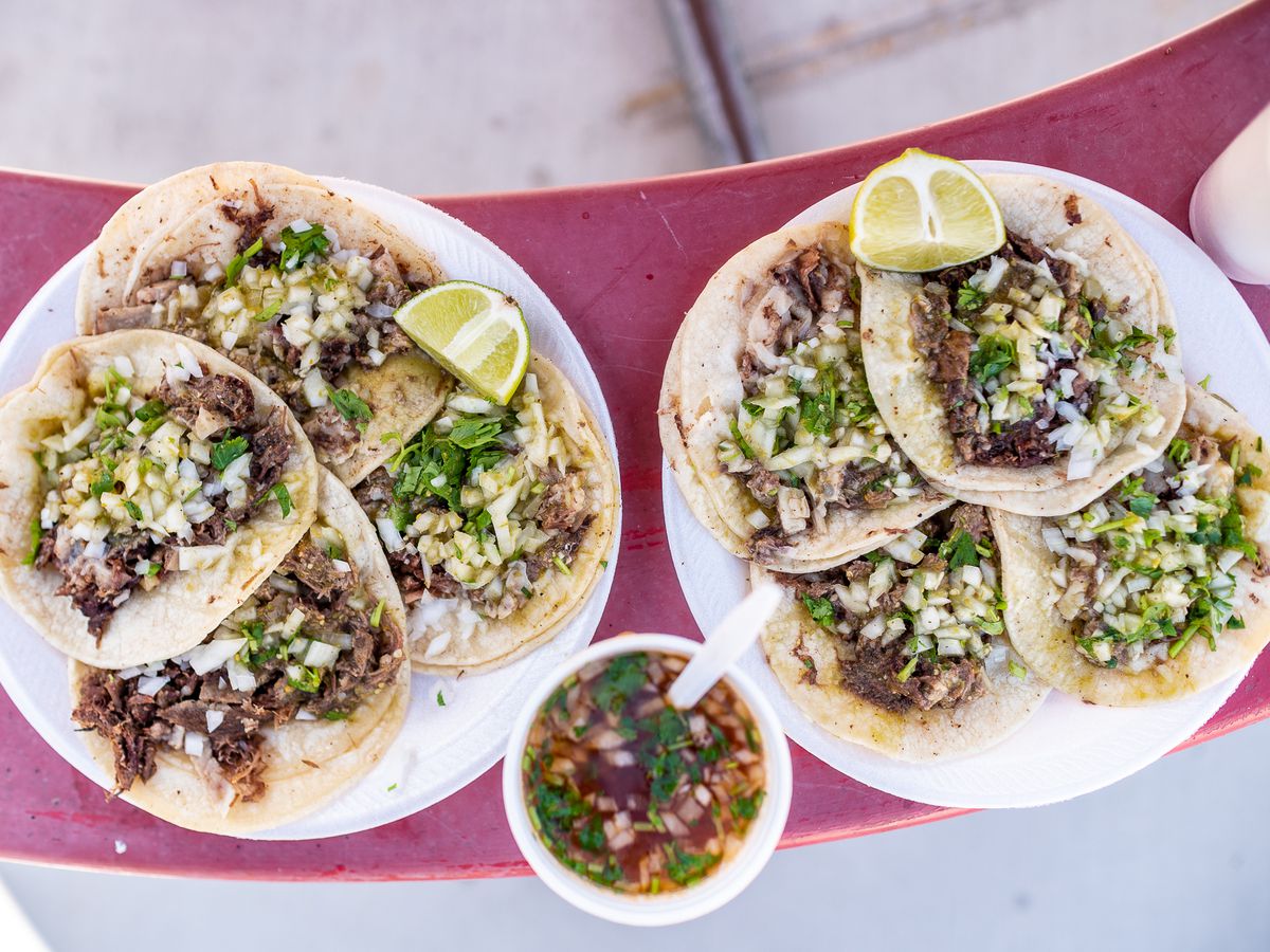 Two plates of loaded tacos de cabeza with a side of spicy, earthy consomé.