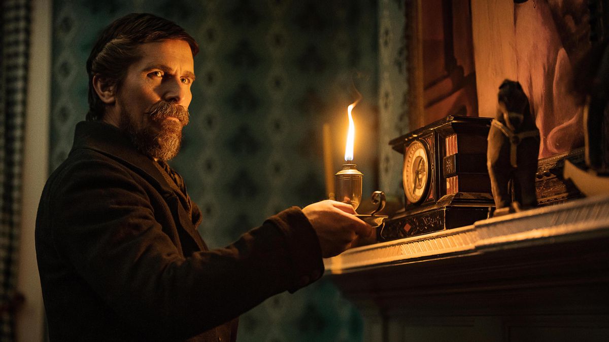 Christian Bale, sporting a great big bushy beard as  1830s detective August Landor, stands by a fireplace with a mantel crowded with bric-a-brac in The Pale Blue Eye