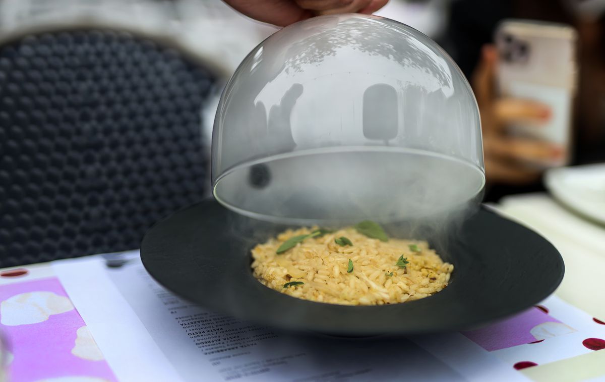 Smoke-filled dome being lifted off a plate of risotto