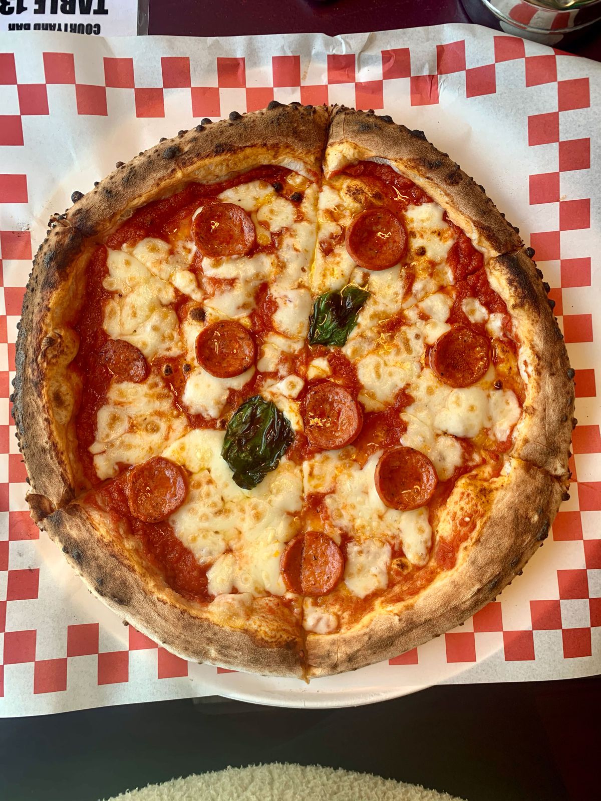 A classic pepperoni pizza on some classic red-and-white checkerboard paper