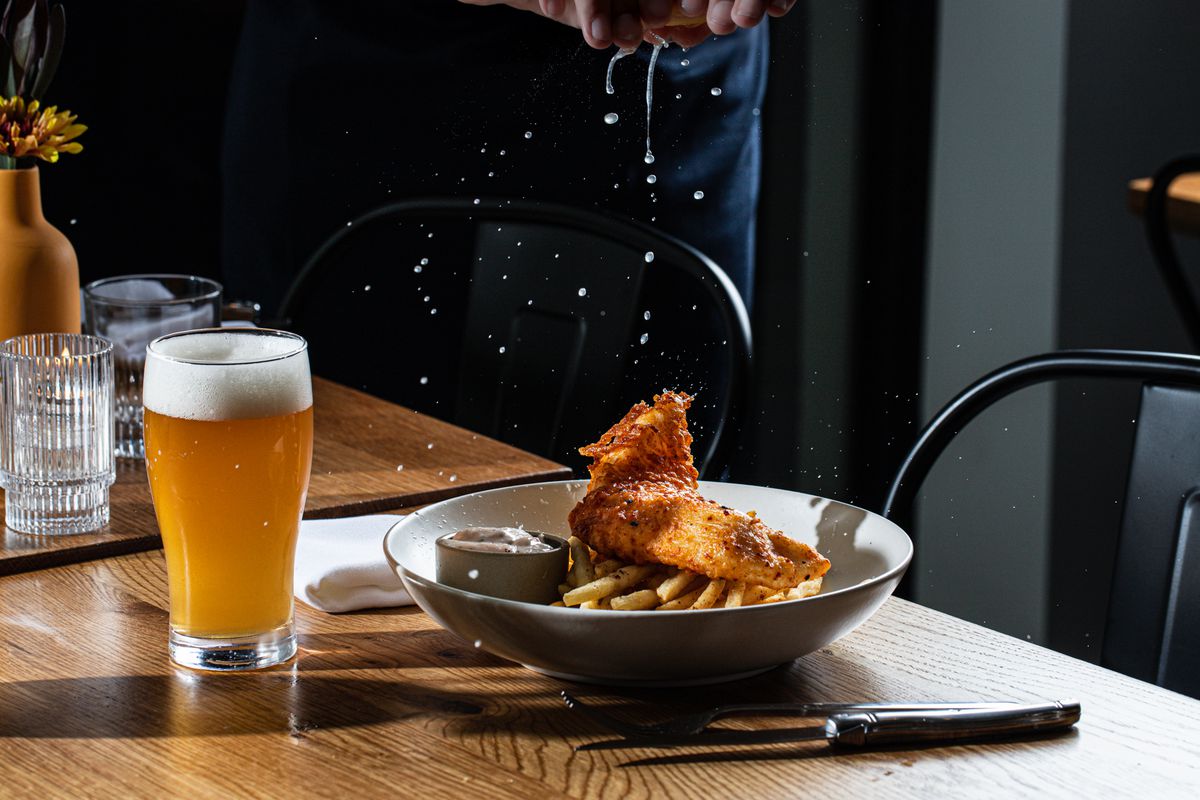 Lemon juice sprinkles down on a bowl containing fish and chips beside a pint of beer at Isla and Co. in Buckhead Atlanta. 