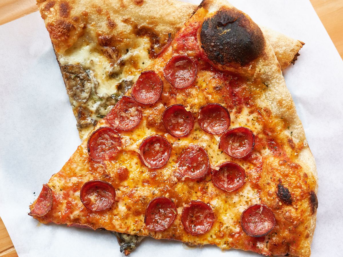 A slice of pepperoni pizza layered on top of a slice of mushroom pizza on a sheet of wax paper