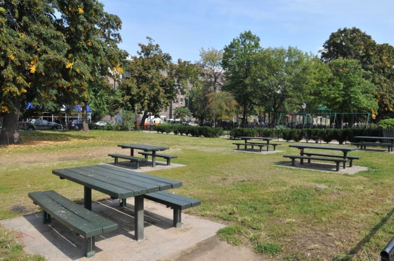 A park with picnic benches, tables, trees, and grass.