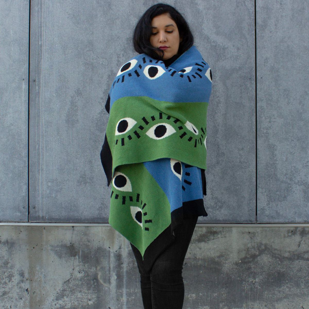 A woman wraps a green and blue blanket with eye motif around her body 