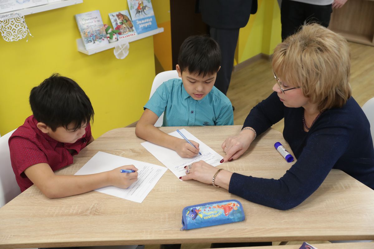A teacher sits at a work table with two young students.
