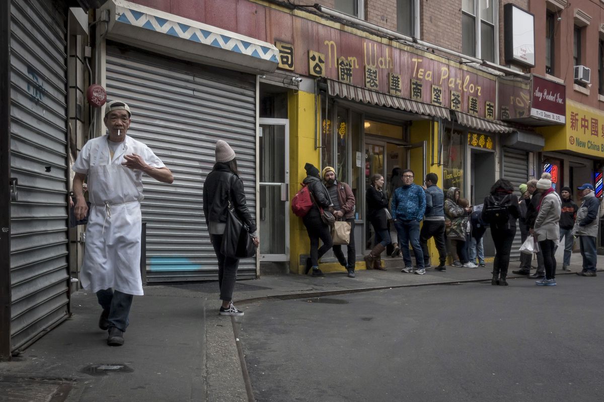 A chef hustles in the foreground as a knot of customers wait in the background on a darkened Doyers Alley.