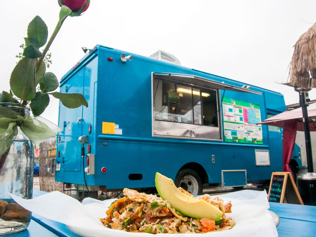 A taco with eggs and an avocado slice on a blue basket lined with wax paper in front of a blue food truck.