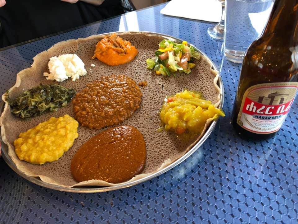 Meskel’s injera topped with vegetables and meat, next to a bottle of beer.