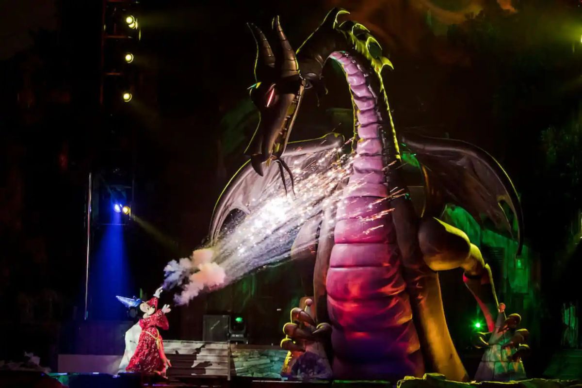 Mickey Mouse wearing a wizard costume and firing sparks at a dragon in a Disneyland show