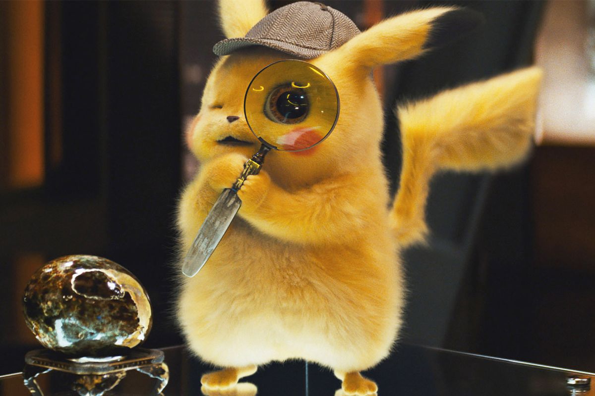 Detective Pikachu holds up a magnifying glass to his left eye while standing on a fancy desk