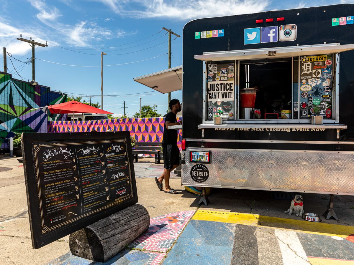 A customer orders food outside of the Detroit 75 Kitchen food truck on a sunny day during summer 2020.