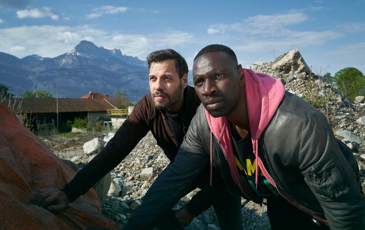 Laurent Lafitte and Omar Sy crouch behind a pile of rock and rubble in The Takedown