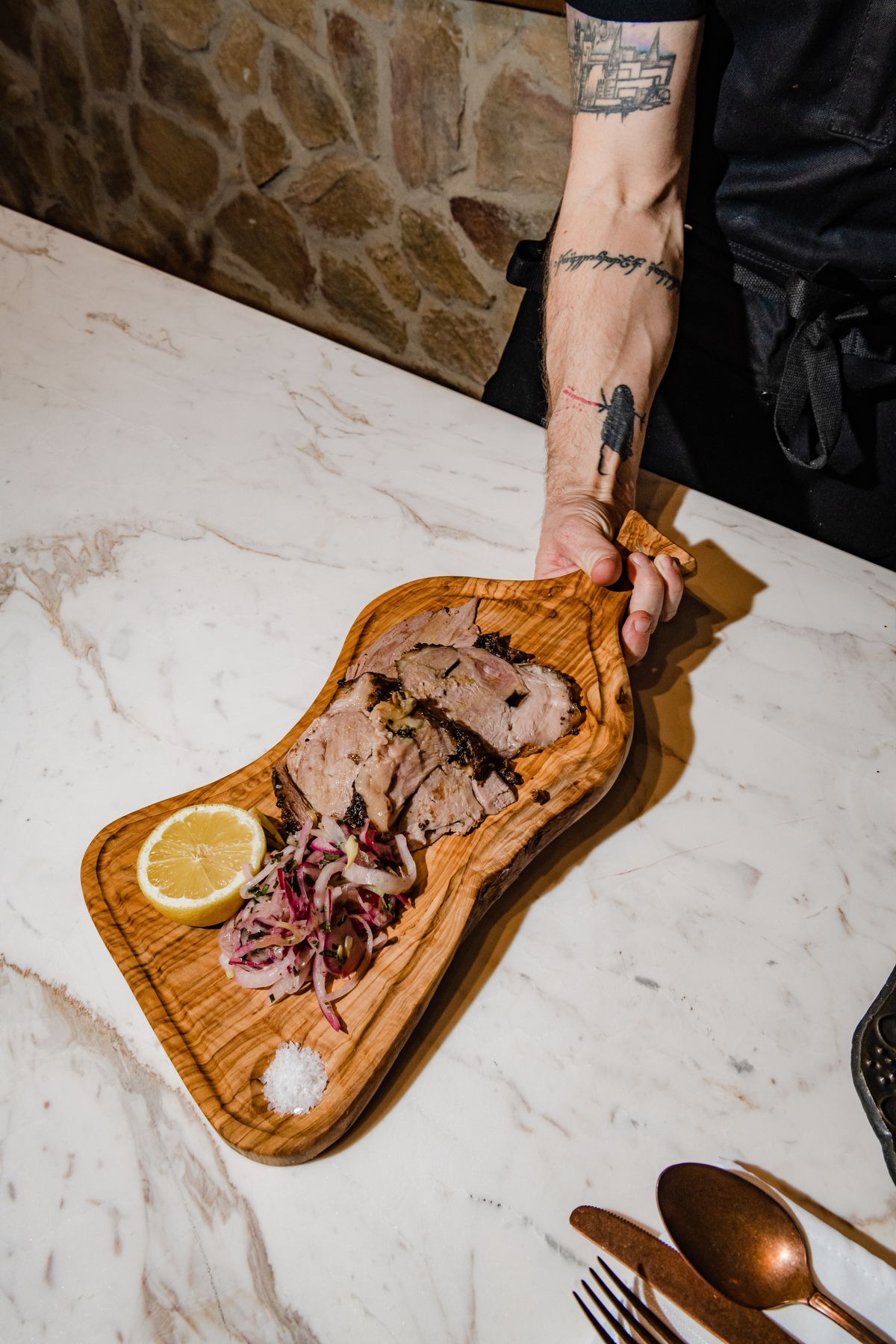A wooden slab filled with lamb pieces, relish, a lemon half, and flaky white salt.