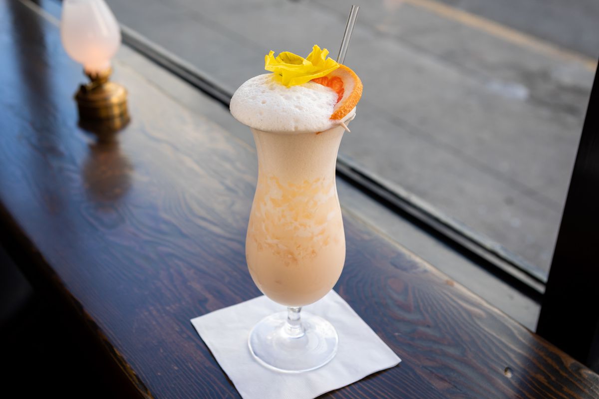 A foamy cocktail in a fluted glass with an orange wheel garnish.