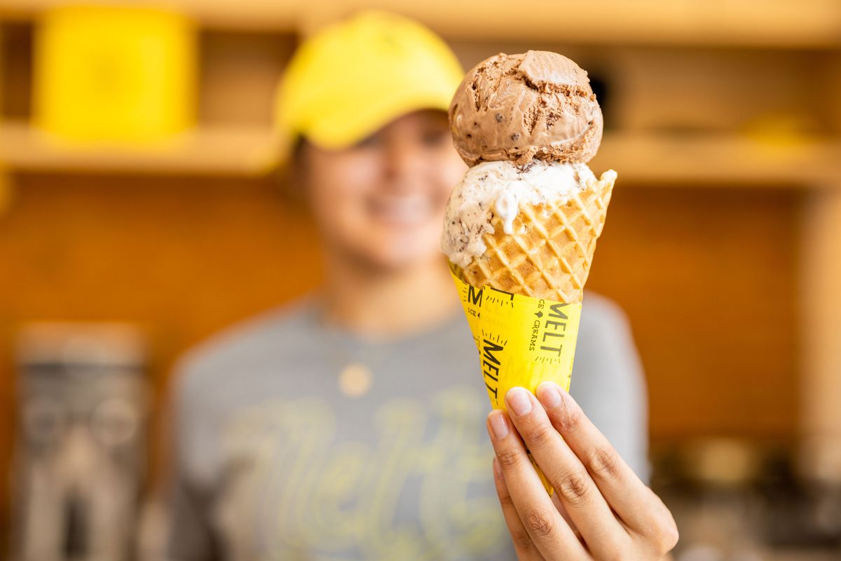 A woman in a uniform holds out a double scoop ice cream in a waffle cone.