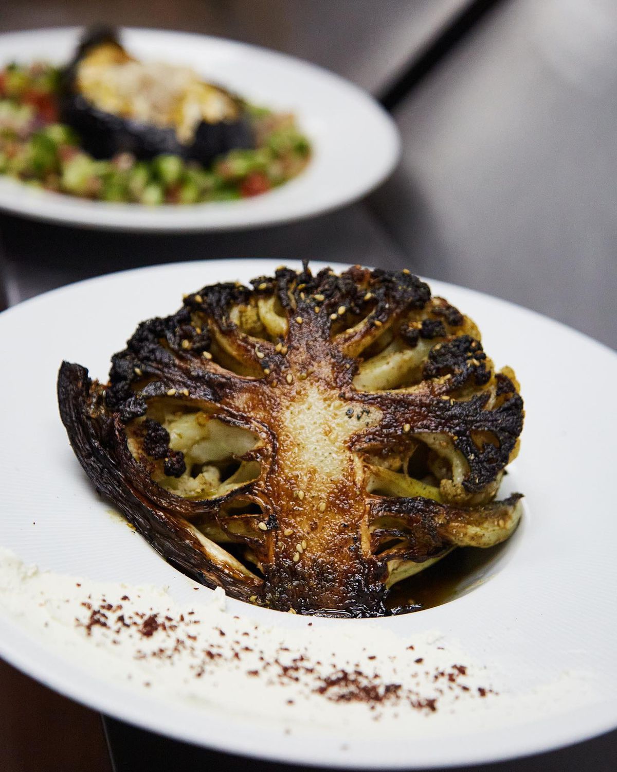 A head of cauliflower is roasted whole in a brick oven and served alongside house labneh and doused in za’atar spice, creating an intoxicating aroma of smoky, earthy herbs from Nur Kitchen on Buford Highway in Atlanta. 