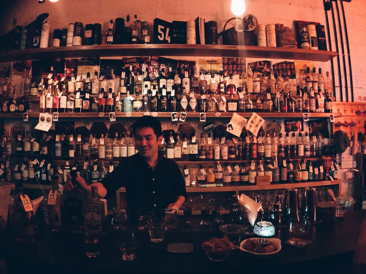 A bartender stands in front of a wall of bottles.
