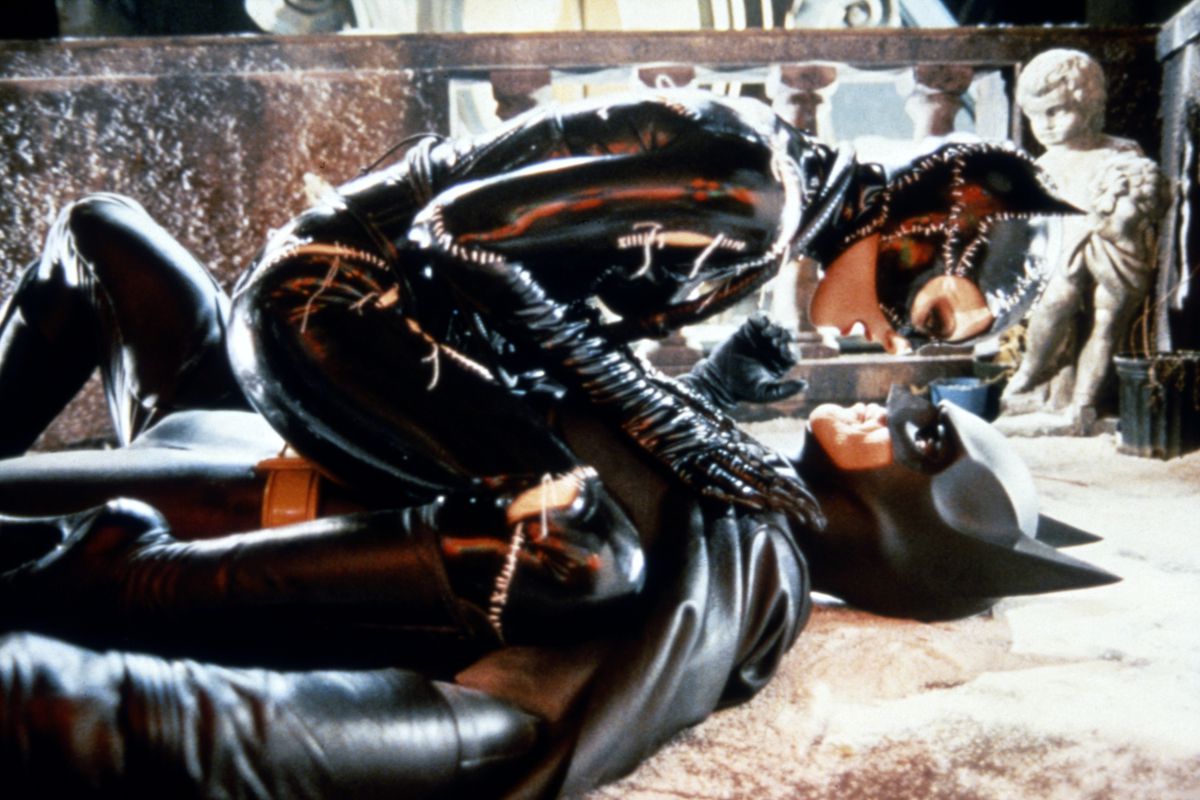 Michelle Pfeiffer as Catwoman crouched face to face on top of Michael Keaton as Batman, who is flat on his back on the floor.