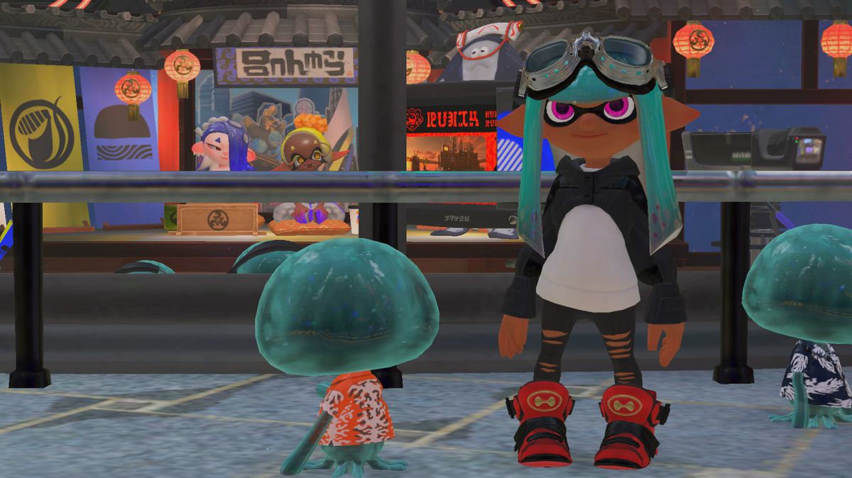 A teal inkling standing in front of some shops in the city area of Splatoon 3. The inkling is wearing pilot-style googles, a white shirt with an extremely cropped black hoodie over it (resembling an orca), and chunky red-and-black hi-top sneakers.
