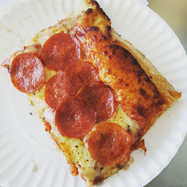 Closeup of a single slice of Sicilian pizza, topped with pepperoni, on a white paper plate