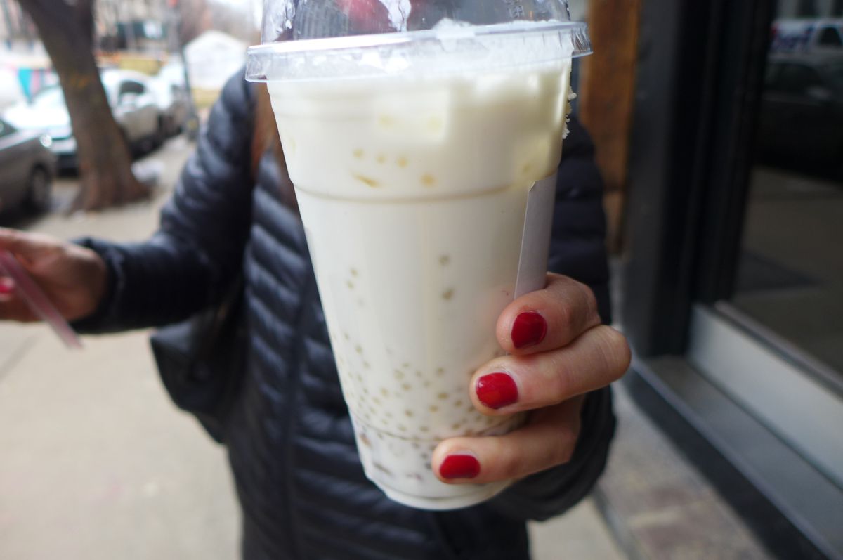 A hand with red-painted nails holds a glass of white bubble tea.