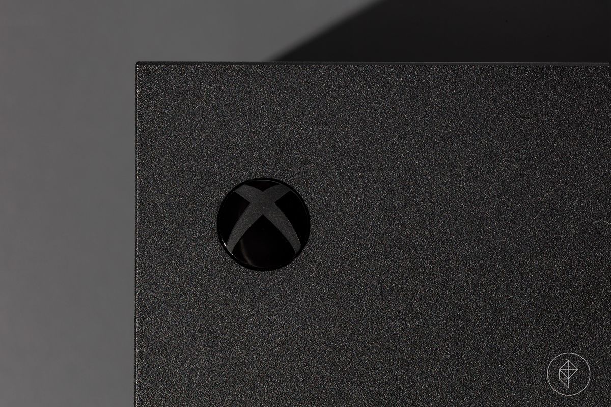 close-up of the Xbox power button on an Xbox Series X video game console photographed on a dark gray background