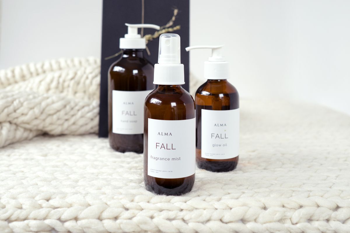 Four brown glass bottles with clean white labels in a fine line font that reads Alma, on a white background on top of a white chunky knit blanket