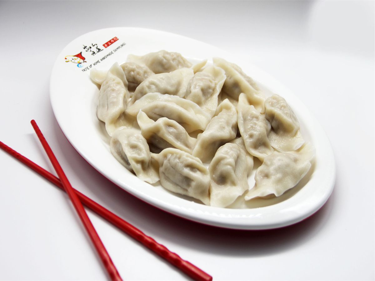 A plate of steamed dumplings next to a pair of red chopsticks.