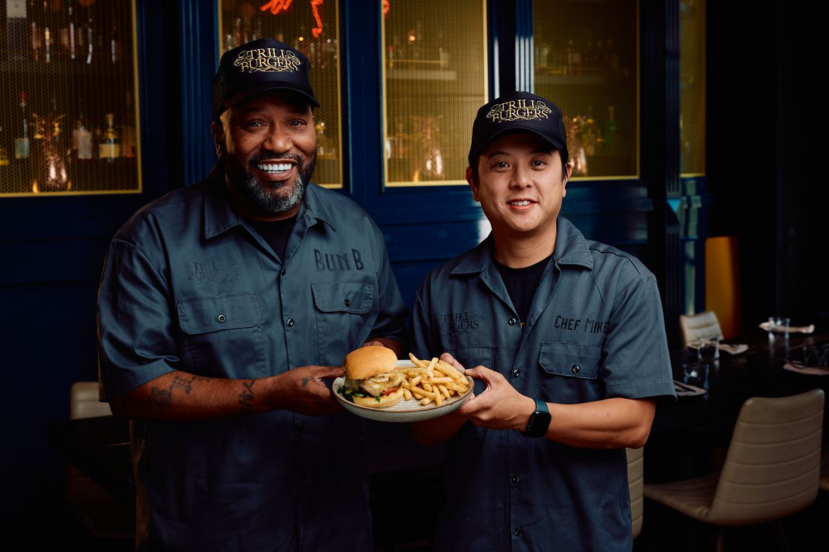 Bun B and Mike Pham pose holding a plate with a Trill Burger and fries.