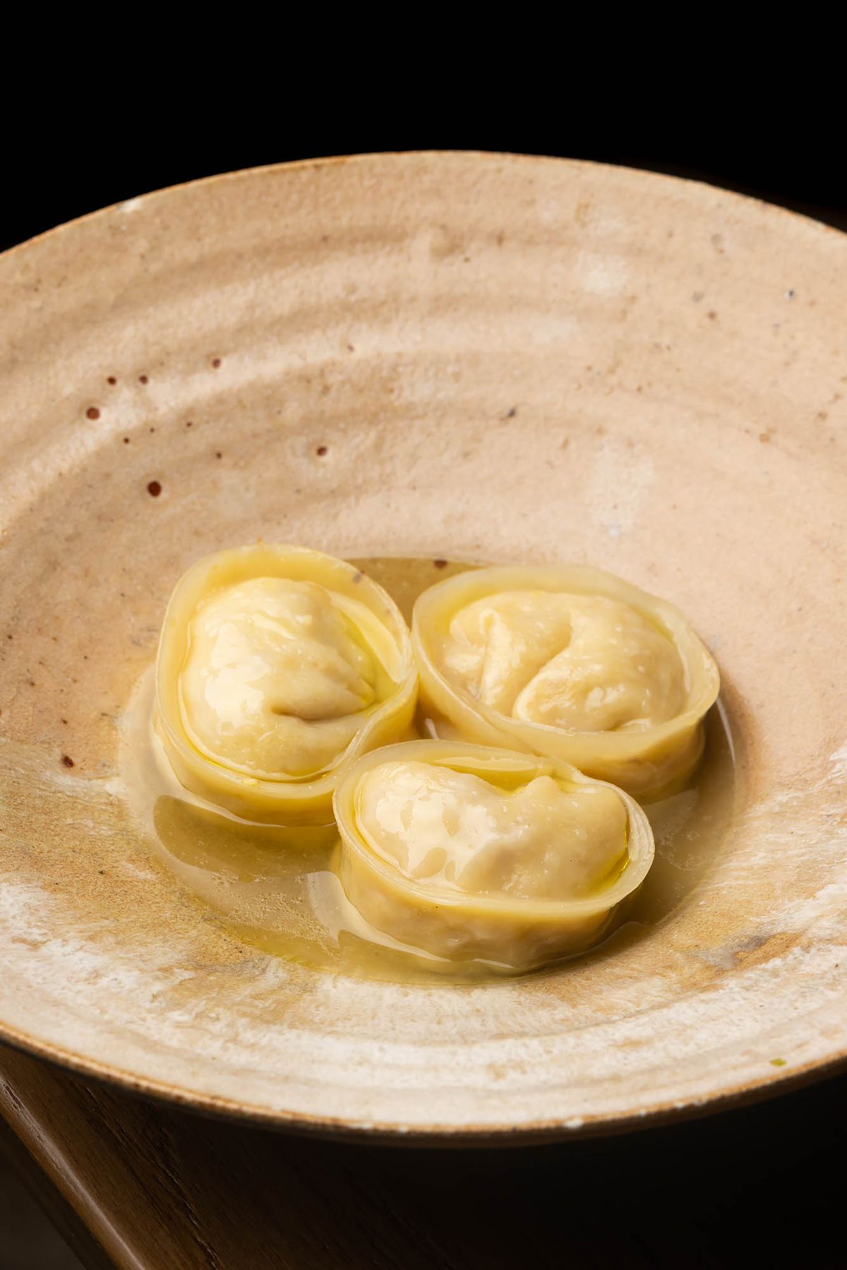 Three dumplings in a clear broth on gray stoneware at LA restaurant Yangban.