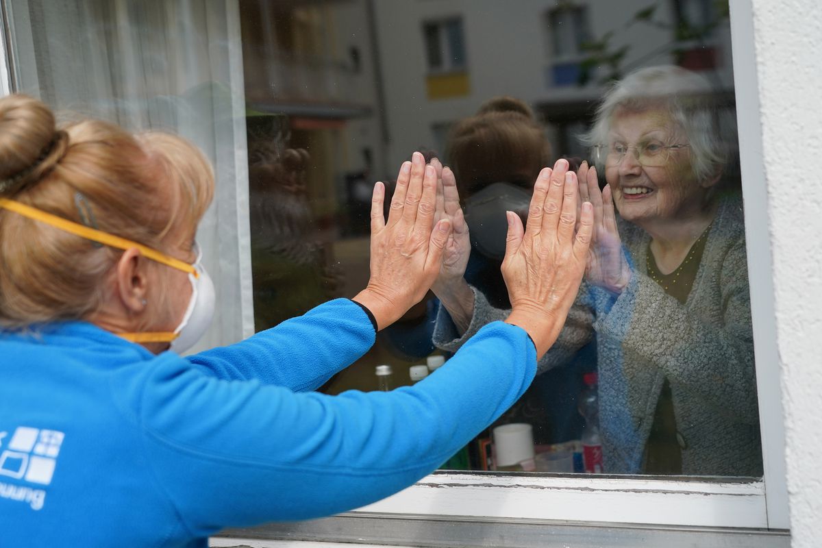 A 90-year-old nursing home resident touches her window to make contact with a caregiver. 