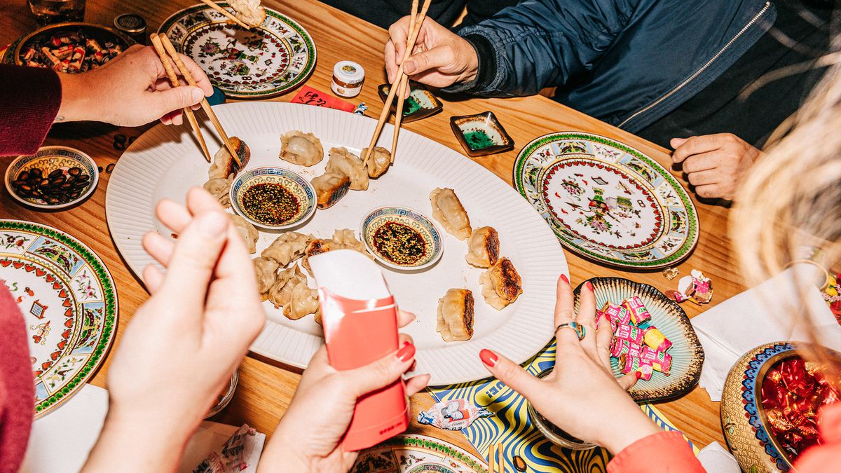 A group of people gather with chopsticks around a big platter of dumplings. 