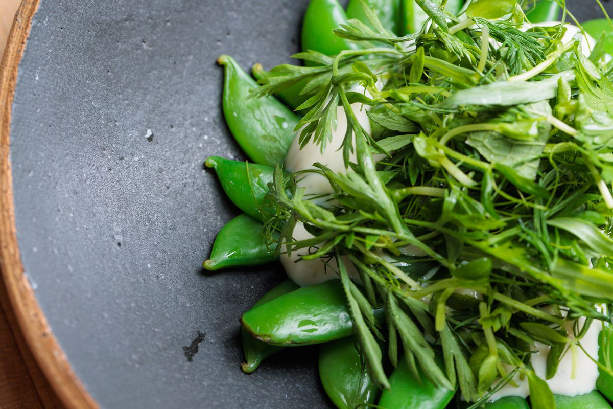 Sugar snap peas lie on a gray plate underneath tofu and herbs