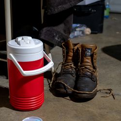 5:21 p.m.: Jimy Hernandez’s work boots and water jug rest in the garage after the day’s work. Jimy works full time for an asphalt paving company.