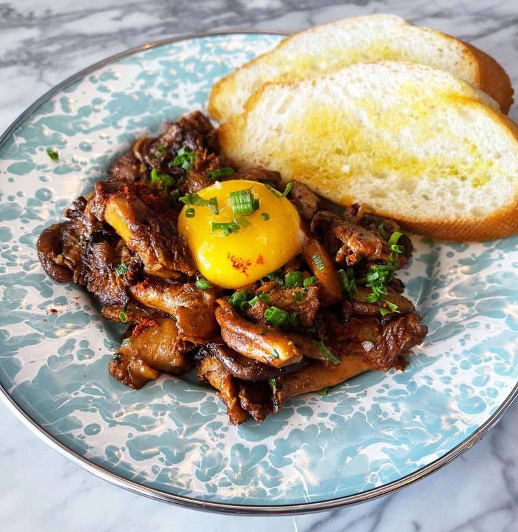 Sauteed mushrooms with an egg yolk on top and slices of baguette.