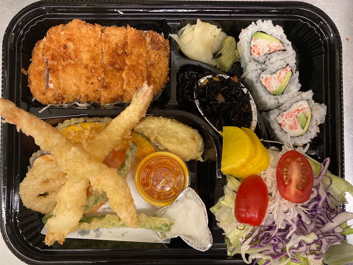 A bento lunch with tempura, tonkatsu, sushi rolls, and salad