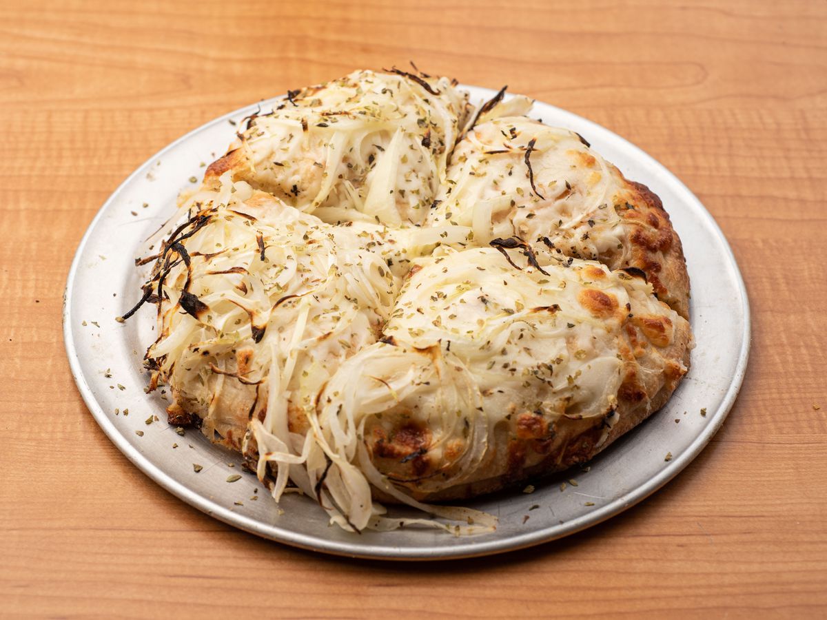 A side angle view of an extra-oniony pizza with lots of cheese on a metal plate.