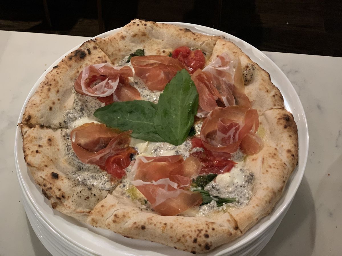 A round pizza with basil leaves, prosciutto and more.