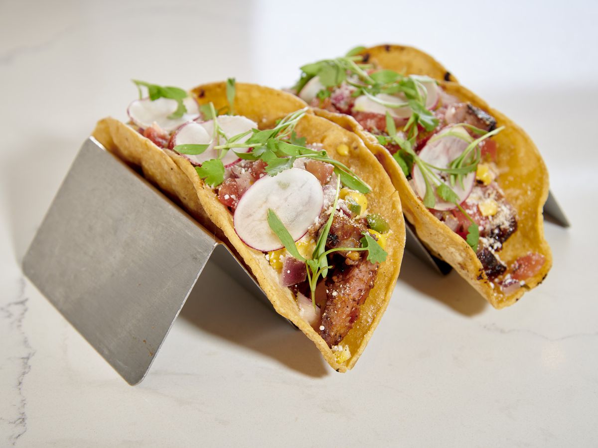 Two tacos dressed and laid out on metal holders.
