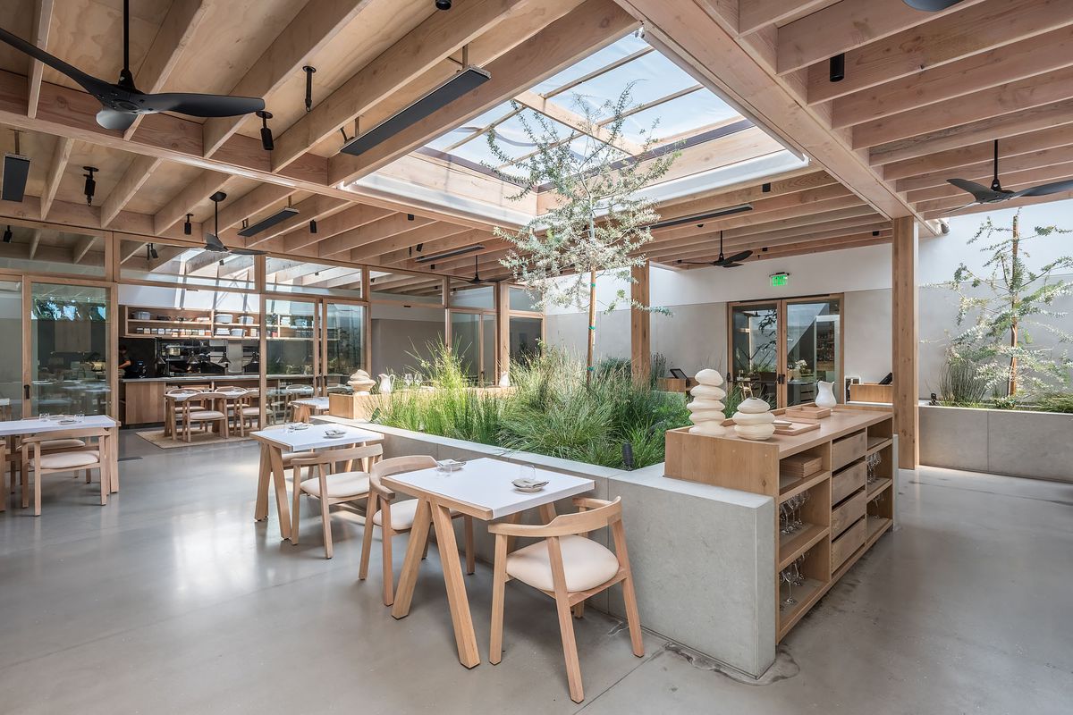 Dining room inside Auburn with skylight, wooden rafters, and grey concrete floors with foliage.