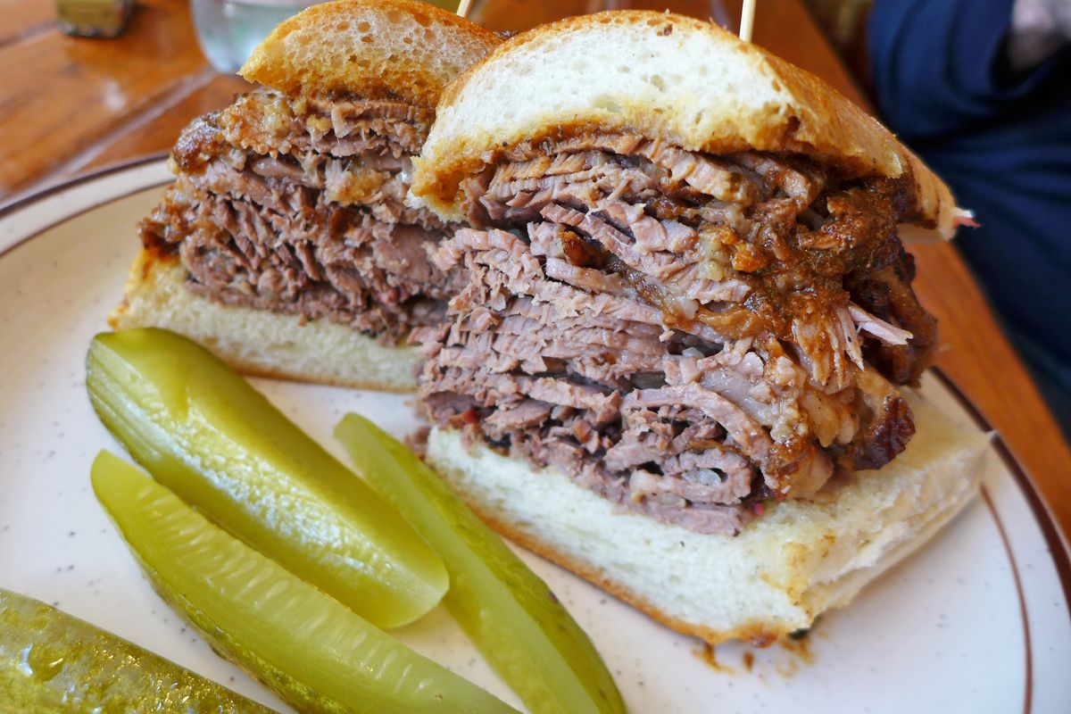 Two halves of a brisket sandwich on a club roll with gravy, accompanied by four pickle spears