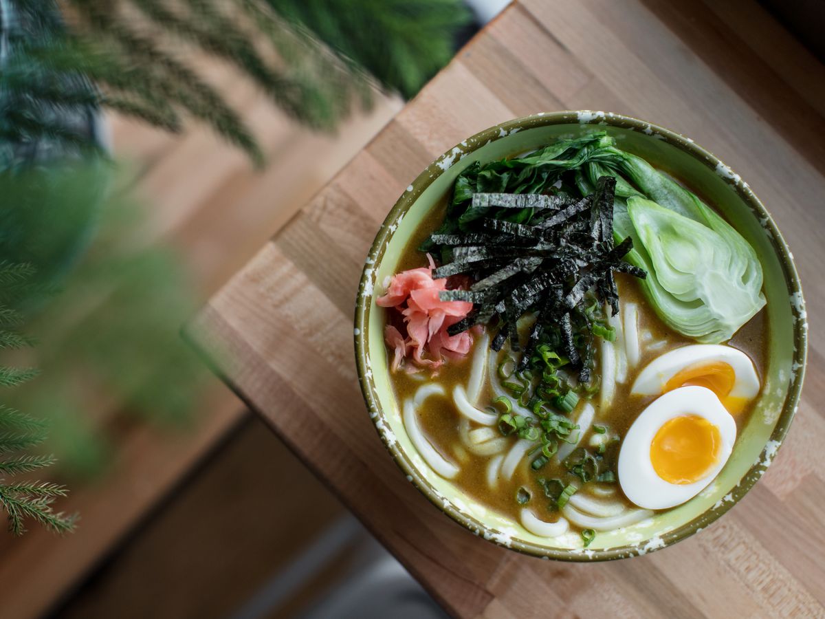 A bowl of udon noodles with boiled eggs, green nori, baby bok choy, and pink pickled radishes at Ima in Corktown.
